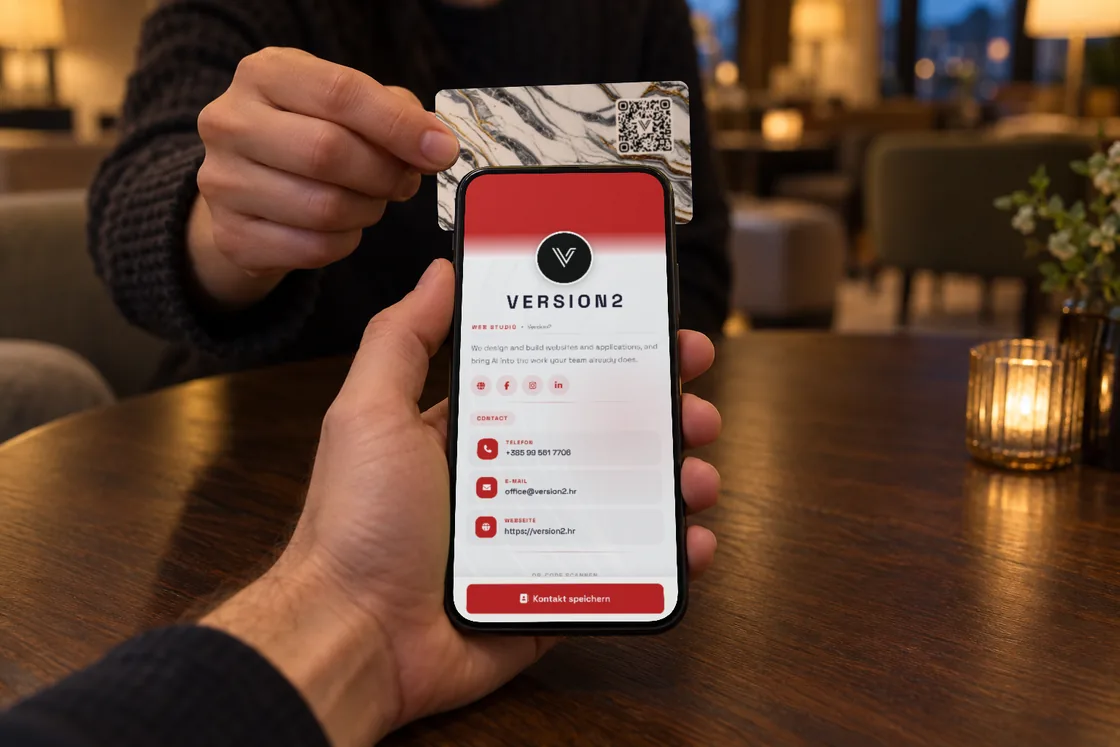 Eine Karte im Design Goldmarmor, über den Tisch an die Rückseite eines Smartphones gehalten, auf dem Bildschirm schon das Version2-Profil, das sie öffnet.