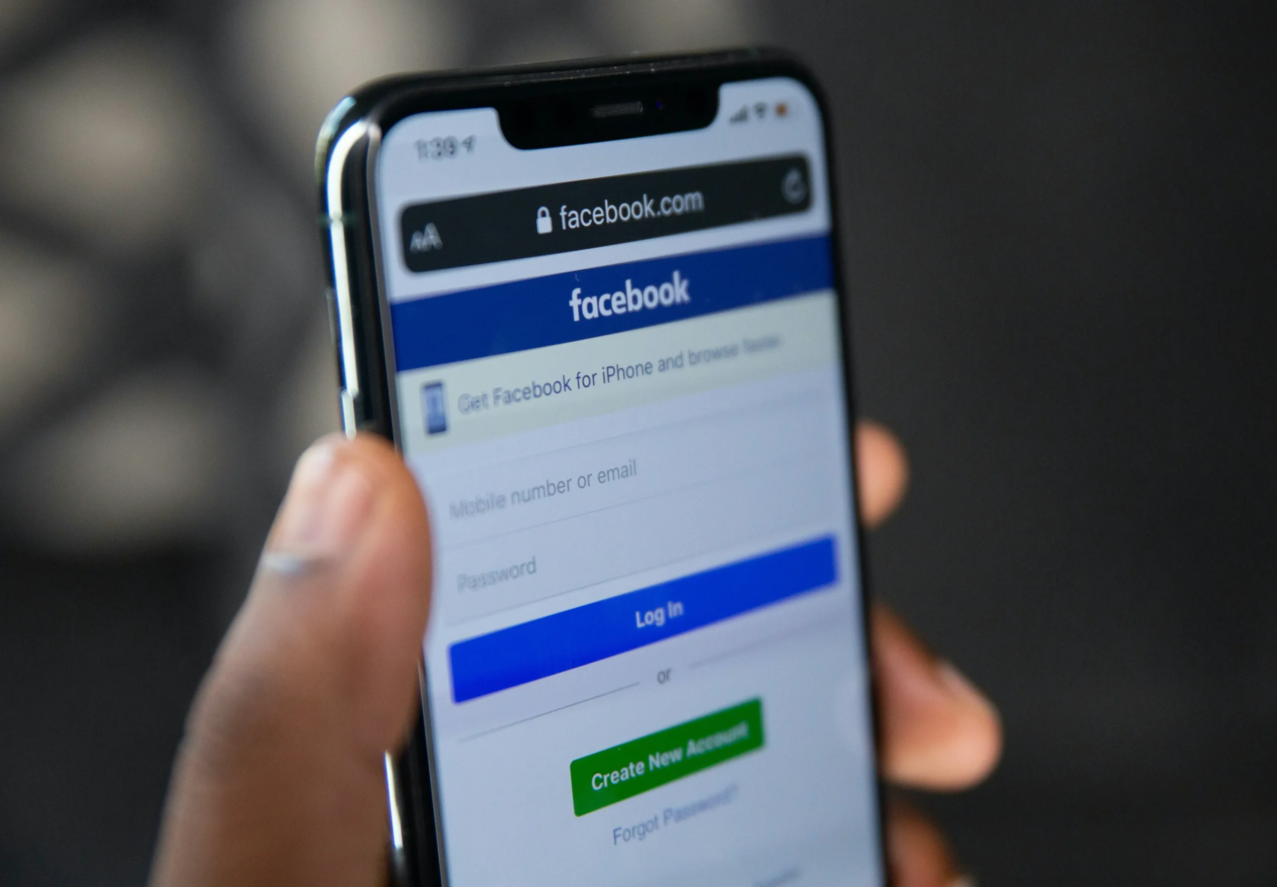 Nahaufnahme einer Hand, die ein Smartphone mit geöffnetem Facebook-Anmeldebildschirm hält.